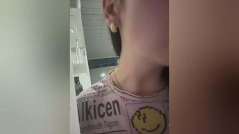 A video captures a woman with a short, dark ponytail, wearing a \"Kicken\" T-shirt, standing beside a medical infusion pump in a dimly lit room.