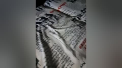 A close-up video of crumpled newspaper pages, predominantly white with black text, partially obscured by creases and folds, giving a sense of hurriedness and chaos.