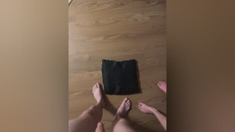 A video of two people's bare feet on a wooden floor, with a black cloth placed centrally between them. The background is beige.