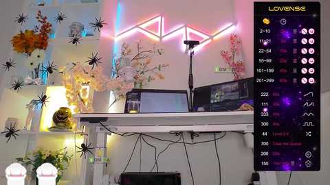 Video of a modern, colorful room with a white desk, black computer monitor, and pink neon lights; shelves hold plants, a gold Buddha statue, and a white statue.