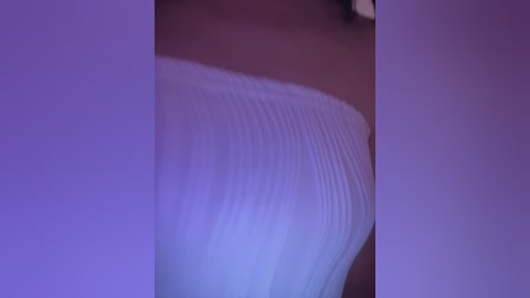 A close-up video of a white, ribbed, textured fabric, possibly a piece of clothing, illuminated by soft, purple lighting, creating a dreamy, abstract effect.