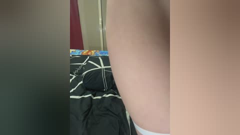 Video of a woman's bare right shoulder and upper back in a dimly lit room with a black and white patterned bedspread.