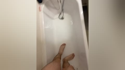 Video of a nude person in a bathtub, legs crossed at the ankles, feet submerged in water, with a showerhead above.