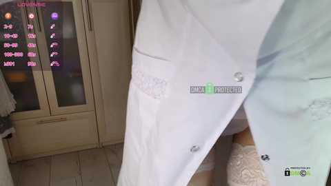 Video of a person wearing a white lab coat with a logo and a green patch, standing in a modern kitchen with beige cabinets, a digital display, and a white countertop.