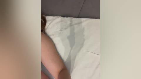 Video of a person lying on a white sheet, partially covered by a gray blanket, with only their arm and shoulder visible, capturing a casual, intimate indoor setting.