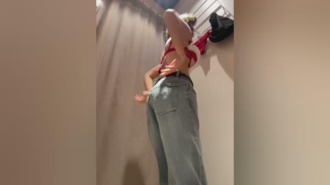 Video of a blonde woman in a red crop top and high-waisted light blue jeans, captured from a low angle, emphasizing her curvy figure and buttocks.