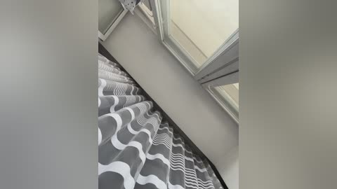 Video of a modern bathroom ceiling with white and grey wavy patterned shower curtain, white-framed window, and white ceiling fan.