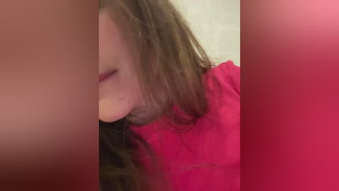 Video of a woman with shoulder-length brown hair, partially obscured by pink and beige text boxes, wearing a red shirt, with a blurred background.