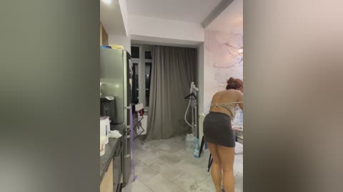 Video of a modern, dimly lit gym with beige walls, a woman in a black sports bra and shorts, a treadmill, and a water dispenser.