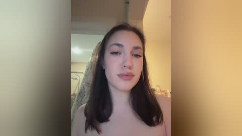 Video of a fair-skinned woman with long, dark brown hair, wearing a sheer veil, posing indoors with a soft, yellowish lighting.