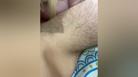 A close-up video showing a person's upper arm with a visible mole and slightly hairy skin, partially covered by a patterned fabric, likely a bed sheet.