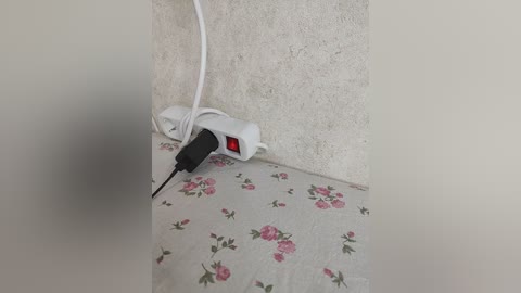 A video showing a white power strip plugged into a wall socket, with a black USB cable inserted, positioned on a floral-patterned cloth. The background is a textured, beige wall.