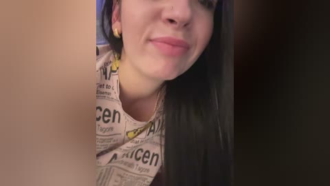 A close-up video of a smiling woman with long black hair and pale skin, wearing a \"The Times\" newspaper shirt, partially obscured by a blurred figure.