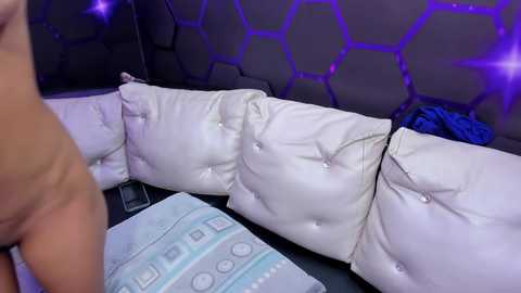Video of a man's bare torso, with a white, tufted leather sofa and hexagonal-patterned purple wall in the background.