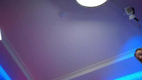 Video of a modern ceiling with a circular light fixture, blue lighting, and a partial view of a person's face.