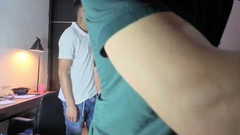 A video shows a man in a teal shirt and jeans in a dimly lit room, facing a woman in a white shirt.