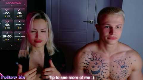 A video shows a shirtless, muscular, tattooed man and a blonde woman with a black top. Both look at a screen displaying \"Love Island\" stats.