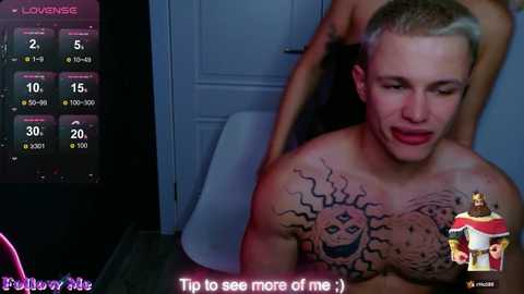 A photo of a shirtless, muscular man with a tattoo of a sun on his chest, sitting in a dimly lit room, with a video game interface showing stats in the background.