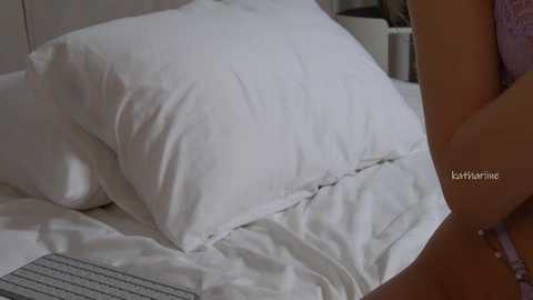 Video of a neatly made bed with white pillows and a lavender blanket, partially visible woman in lingerie, watermark \"KittyYamie.\