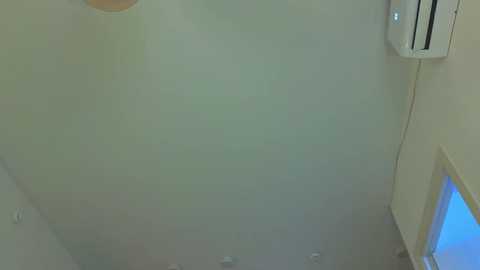Video of a small, dimly lit, beige-tiled bathroom with a fogged-up shower enclosure, an air conditioner on the wall, and a blue-tinted window partially visible in the background.