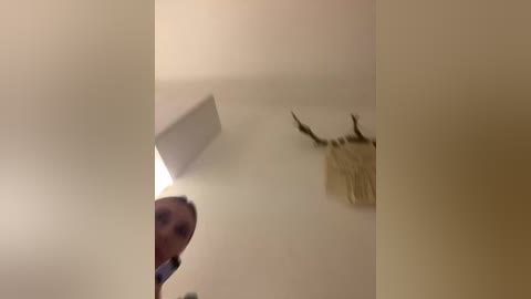 Video of a blonde woman with a light complexion and short hair, wearing a blue top, standing in a dimly lit room. A large, shadowy deer head mounted on the wall is visible in the background.