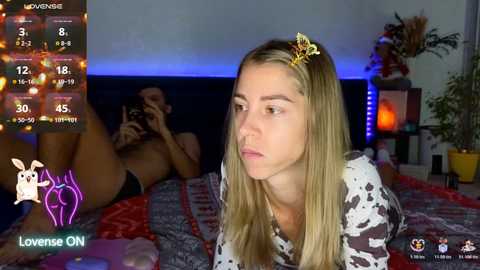 A video of a blonde woman in cow-print pajamas, lying on a bed with a dark-haired woman in lingerie, both on a live stream.