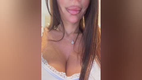 A video of a woman with long brown hair, fair skin, and full lips, wearing a white off-shoulder top, set against a blurred background.