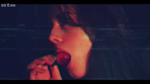 A close-up video of a woman with long, wavy hair, holding a red lollipop near her lips. She has fair skin and a soft, blurred background.