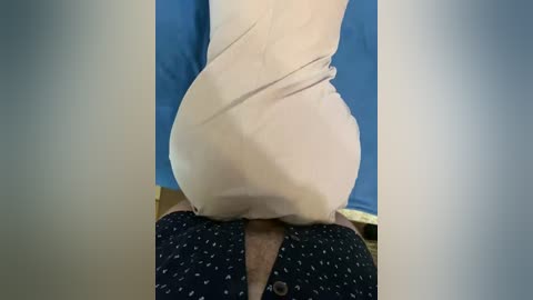 A video showing a person sitting on a white cloth, with a blue wall and dark patterned shirt in the background.