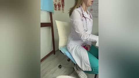 Video of a Caucasian woman in a white lab coat and stethoscope, sitting on a teal chair in a medical exam room with light-colored walls, a calendar, and a blue lamp.