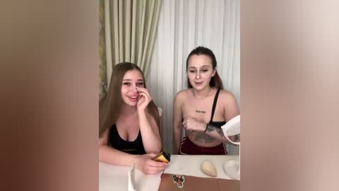 A video of two young women in a bathroom; one with long brown hair, wearing a black tank top, and the other with dark hair in a ponytail, in a black sports bra, applying makeup.