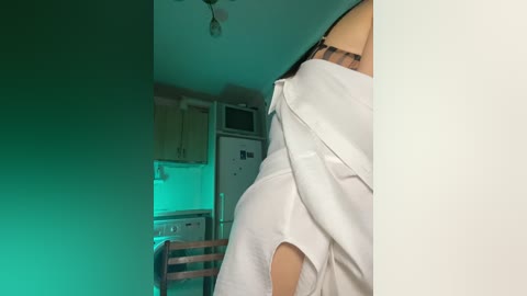 Video of a woman in a white shirt, standing in a dimly lit, modern kitchen with green-tinted lights.