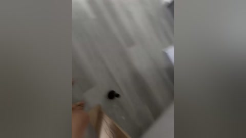 A video depicting a blurred, close-up view of a person's hand holding a small black object, possibly a pen or marker, against a white, textured ceiling. The image is out of focus, with a slight blurriness around the edges.