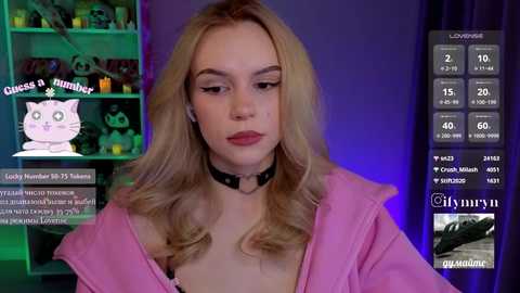 Video of a young woman with blonde hair, wearing a pink jacket, black choker, and makeup, in a room with a cat-themed shelf, live stream overlay.