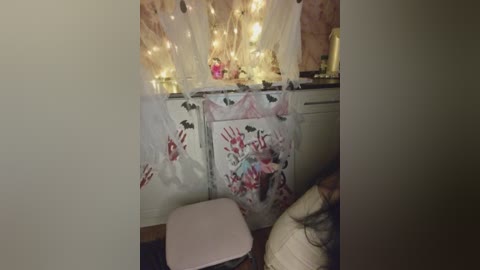 Video of a cozy bedroom with a white dresser adorned with white and pink heart decorations. Fairy lights and sheer curtains create a warm, whimsical ambiance.