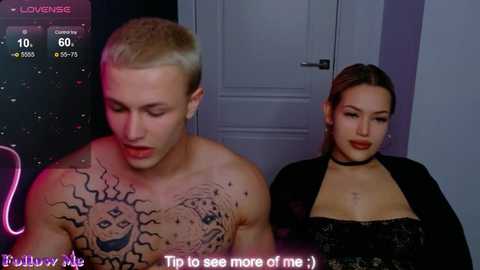 Video of a shirtless man with a sun tattoo and a woman with a choker, both indoors. The man looks down, and the woman smiles. Text reads, \"To see more of me!\
