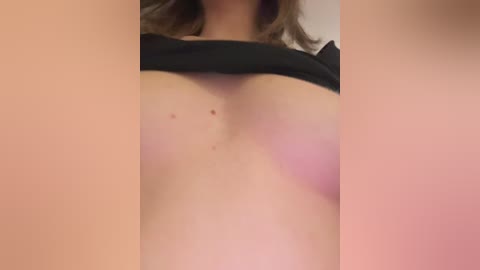 Video of a woman's bare chest, with fair skin and a few moles. She is lifting a black top, revealing her small, round breasts and a pink bra.