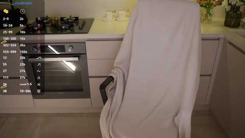 Video of a modern kitchen with a white towel draped over a chair, stainless steel oven and black stove, white cabinets, and a yellow countertop.
