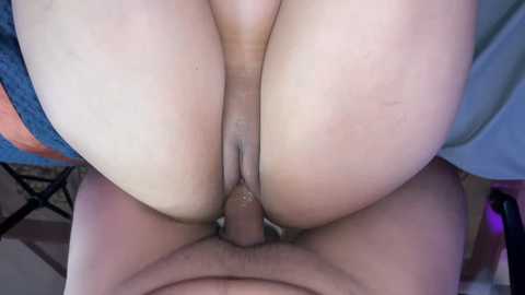 A close-up video showing a penis penetrating a woman's vagina. The woman's large, round buttocks dominate the frame. The background includes a blue and orange fabric.