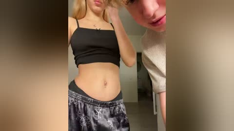 Video of a blonde woman in a black crop top and patterned pajama shorts, with a young girl in the background.