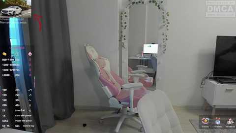 Video of a modern, minimalist gaming room featuring a white gaming chair with pink cushions, a large mirror with green vines, a white TV stand, and a gray curtain.