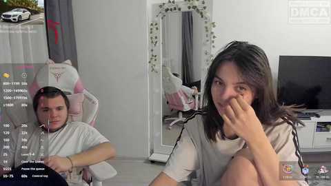 A video captures a young woman with shoulder-length brown hair and a man with short brown hair playing a video game, both sitting in a light-colored room.