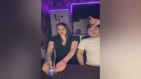 Video of two young people, a woman with long dark hair in a black top, and a man with short dark hair in a white shirt, sitting at a bar with a glass of beer.