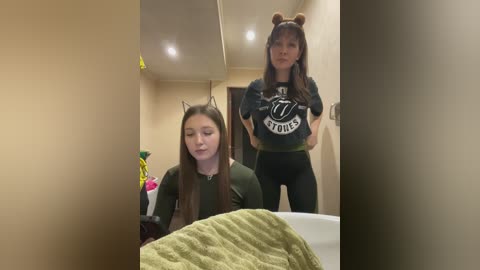 Video of two women in a bathroom; one in a green shirt, the other in a \"Lions\" jersey, wearing cat ears.