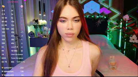 Video of a fair-skinned woman with long brown hair, wearing a pink tank top, sitting on a massage table in a dimly lit room with neon lights, digital watch, and a bottle of lotion.