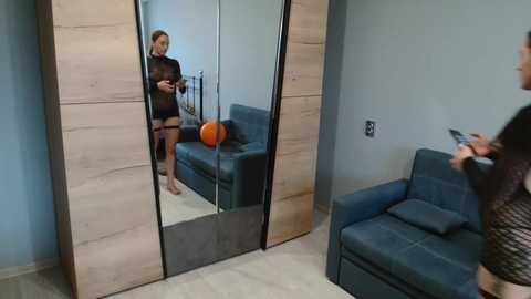 Video of a woman in black lingerie standing in front of a mirror, reflecting her and a blue couch with an orange ball, in a modern, minimalist room.