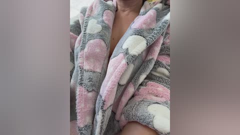 Video of a person wearing a fluffy, pink and white polka-dotted robe, showcasing a soft texture and cozy feel. The image is cropped from the shoulders down, with a blurred background.