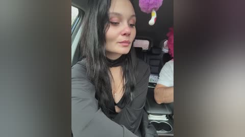Video of a young woman with long black hair, wearing a black choker and top, sitting in a car, with a purple balloon in the background.