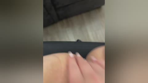 A blurred video of a person wearing black underwear, sitting on a dark sofa with a light wooden floor. The image is grainy, making it difficult to discern details.