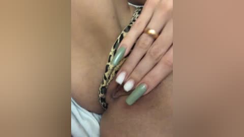 Video of a close-up of a person's hand with long, manicured nails, touching a leopard-print chain necklace. The background shows a tan, smooth skin surface, possibly a thigh.